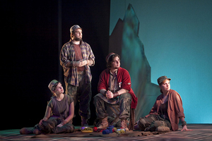 A scene from a modern interpretation of As You Like It—four characters look to the right against a stark blue background, the floor littered with discarded cans.