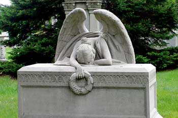 A photograph of a grave stone that has a statue of a weeping angel hunched over it