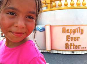 A photograph of a little girl standing near a sign that reads: “Happily Ever After“.