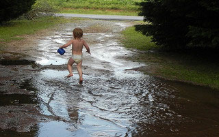 A photograph of a toddler splashing through her feet in puddles