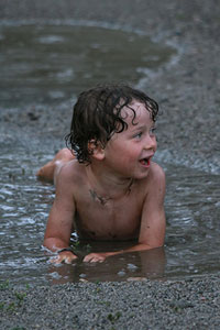 A photograph of a young boy playing in a mud puddle.