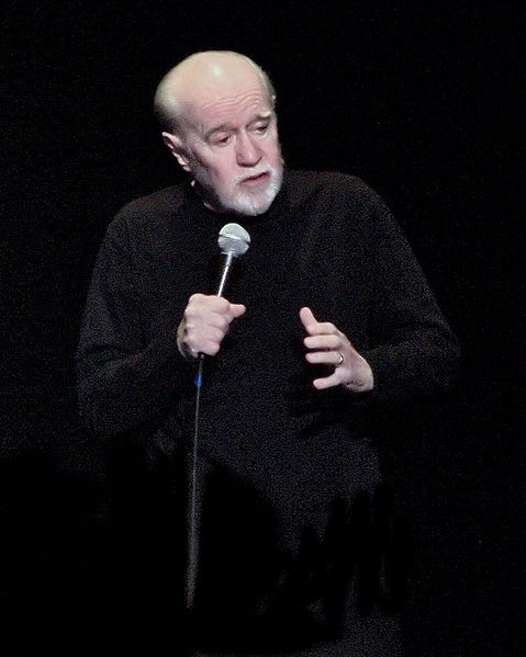 A photograph of the comedian George Carlin on stage addressing the audience