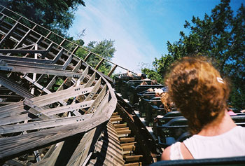 photo of a rollercoaster turning corner taken by someone who is riding it. The back of a woman’s head and shoulders are visible.