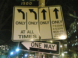 A confusing array of signs on a city street corner that direct traffic using arrows, words, and times.