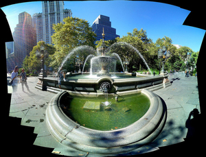 A photograph of a city park fountain near a collection of buildings