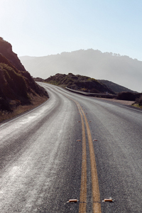 A photograph taken on Pacific Coast Highway 1 in California. It is a winding road going up into the hills.