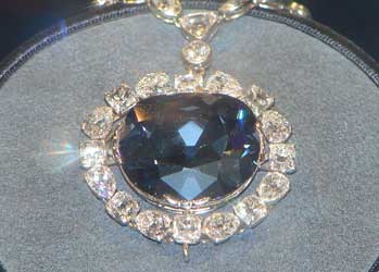 A photograph of the Hope Diamond. It is in a display case. The diamond itself is mounted as a pendant and surrounded by other diamonds on a necklace.