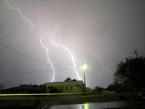 A photograph of lightning bolts striking near a house during a storm.