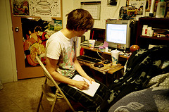 a student in pajamas in a crowded, busy room works on his homework