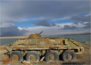 Abandoned, graffitied, and rusted tank mired in soil near a lake