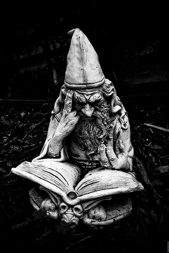 Photo of a statue or stone figurine: a focused wizard sits staring into a large book