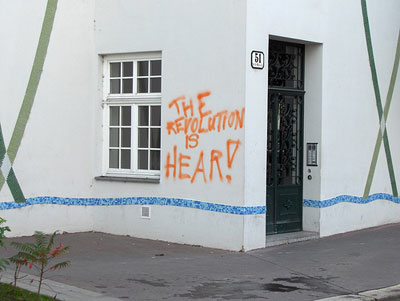 photo of a spraypainted message on a wall that reads “The revolution is hear”