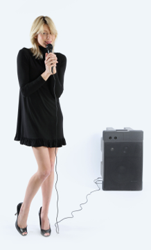 Photo of a girl with shy posture speaking into a microphone.