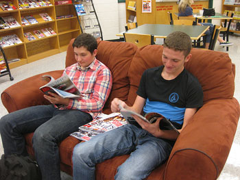 A photograph of two young men looking at magazines in a library.