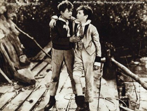  A photograph from the 190 film “Huckleberry Finn”. It shows Huck Finn and Tom Sawyer having a serious discussion. One has the other in a friendly embrace.