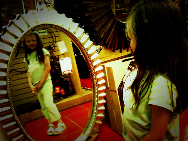 A photograph of a young girl looking at herself in a mirror