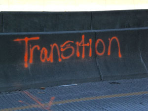 A photograph of a concrete barrier that has the word “transition” spray painted on it 