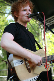 A photograph of pop star Ed Sheeran playing guitar and singing onstage