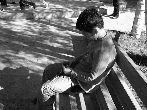 A photograph of a boy sitting on a bench and thinking