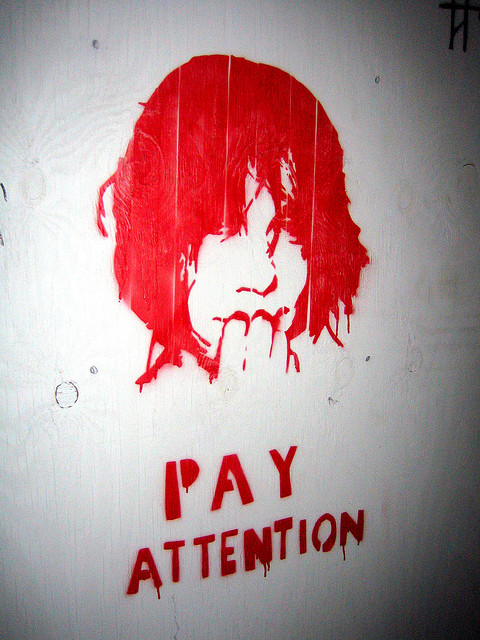 A photograph of a spray painted design featuring a woman’s head with the words ‘pay attention’ underneath it.