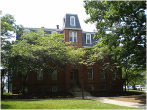 A red brick college building surrounded by trees with a neatly mowed front lawn.