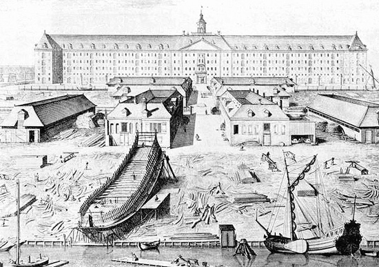 A drawing of an 18th century ship yard in front of an official looking building. In the foreground is a large ships hull under construction with a smaller vessel tied up nearby.