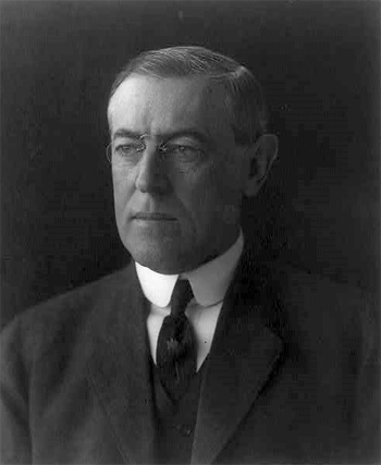 A photograph/portrait of President Woodrow Wilson.  A middle aged man dressed in a suit and necktie wearing glasses.