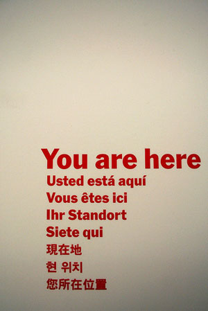 A sign that reads: You Are Here; Usted está aquí, Vous êtes ici; Ihr Standort, Siete qui, and the same message in Chinese, Korean, and Japanese.