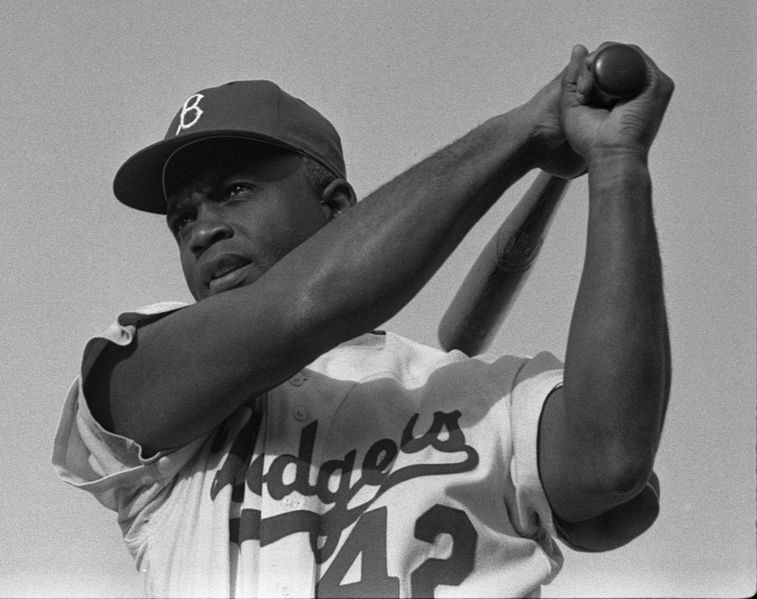 A photograph of Jackie Robinson swinging a bat in Dodgers uniform, 1954.