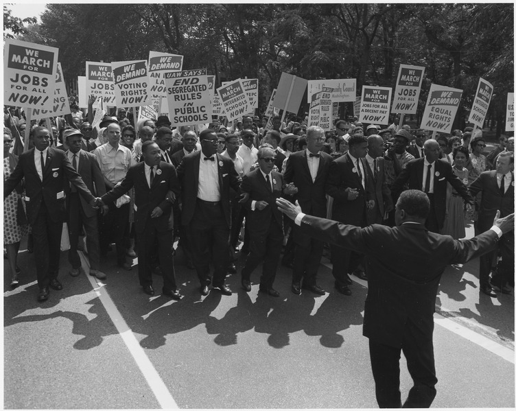 A photograph of a civil rights march on Washington D.C. in 1963; Several prominent leaders are leading them including Dr. Martin Luther King Jr.
