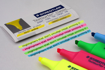 A photograph of a four different colored highlighter pens with their caps off next to some highlighted text
