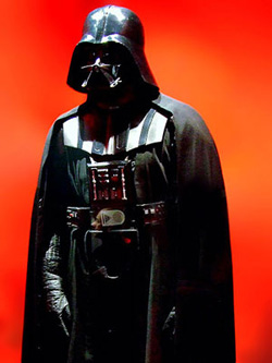 A photograph of Darth Vader, the chief villain in the Star Wars series. He wears a helmet that obscures his face, body armor, and a long cape.