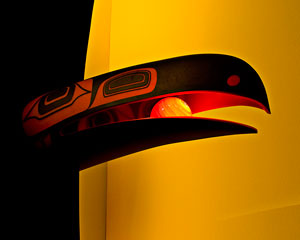 A vivid image in glowing reds and yellows. A huge raven’s beak holds a luminescent yellow sphere.