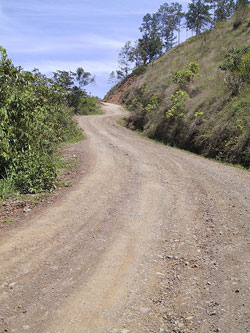 A photograph of a dirt road winding up a hill, into the distance