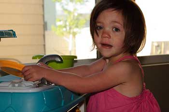 A photograph of a four or five year old girl playing with a toy kitchen set