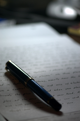 A photograph of a pen laying on a sheet of paper with hand writing on it.