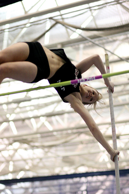 A photograph of a female pole vaulter clearing the bar