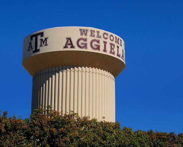 A photograph of the water tower at Texas A&M in College Station. It reads “welcome to Aggieland” with a Texas A&M logo.