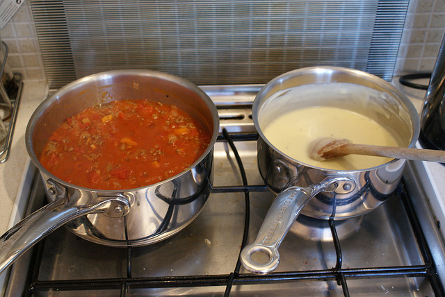 A photograph of lasagna being prepared. Shown are two pots ion a stove: one for the sauce and the other for the pasta.