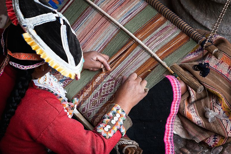 A photograph of an Inca woman weaving textiles at a manual loom.