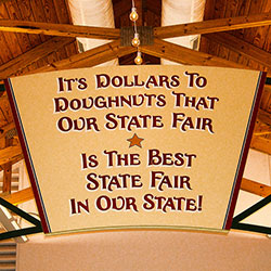 A photograph of a sign that reads “It’s dollars to doughnuts that our state fair is the best state fair in our state.”