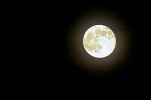 Photo of a bright moon in a dark sky; an aura surrounds the moon.