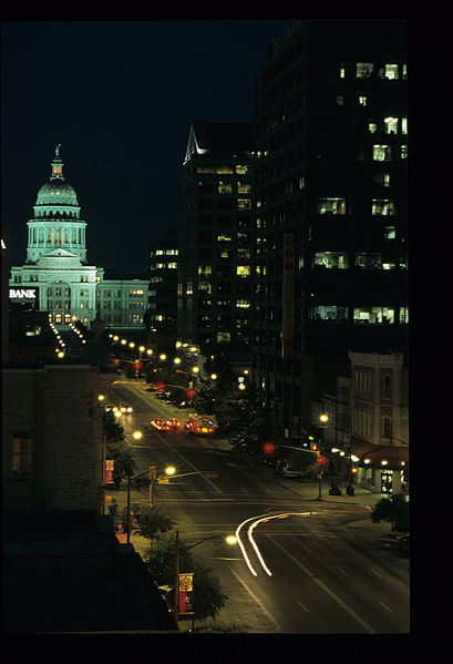 A photograph of Austin, Texas at night. Shown is a portion of Congress Avenue. The Texas Capitol building is visible at the end of the street.