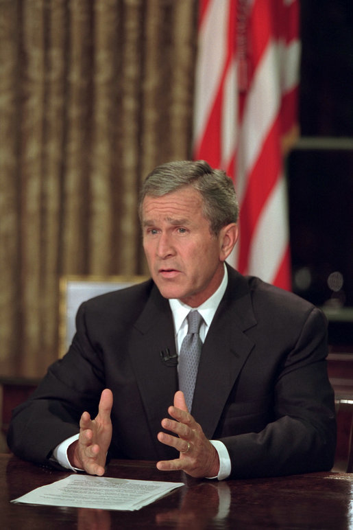 A photograph of President George W. Bush seated in the oval office giving a televised speech following the 9/11 attacks
