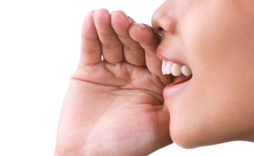 A photograph of a woman’s mouth saying something. She has a hand held up to help amplify her speech.