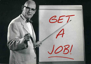 photo of an older man wearing a suit and bowtie; he points at the words “get a job” on chart paper with a long pointer and points his other hand at the camera