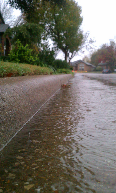 A photograph of rain water running down a street towards a drain.