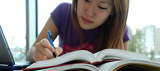A photograph of a female student taking notes and reading from two large books