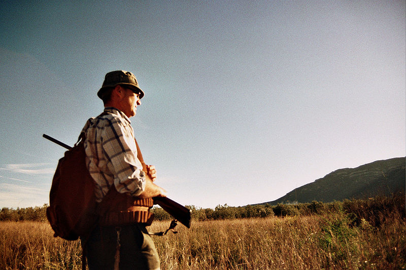 A photograph of a man hunting. He is carrying a shotgun and a game bag