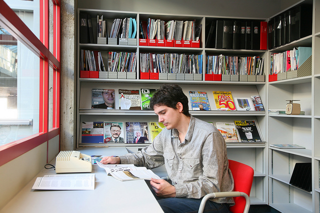 A photograph of a young man doing research in a library periodicals room